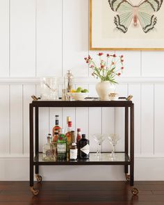 a bar cart with liquor bottles and glasses on it in front of a butterfly painting