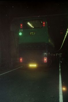 a green bus driving down a street at night with its lights on and the door open