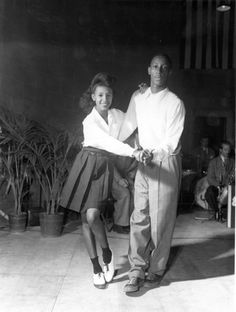 an old black and white photo of a man and woman holding hands while standing on the dance floor