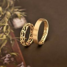 two gold wedding rings sitting next to each other on top of a brown table with flowers