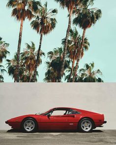 a red sports car parked in front of palm trees and a blue sky with white clouds