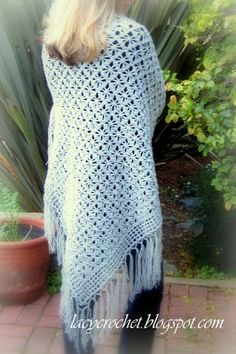 a woman wearing a white crochet shawl standing in front of a potted plant