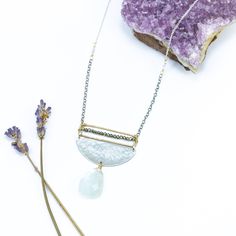 Embrace the enchanting allure of our Moonstone Radiance Necklace, a harmonious blend of celestial elegance and artistic craftsmanship. At its heart, a large moonstone, glowing with an ethereal light, gracefully hangs from a textured silver half circle, capturing the essence of lunar mystique. Above, a delicate gold rectangle, meticulously adorned with tiny sparkling pyrite gemstones, stretches the length of the disc, adding a touch of subtle brilliance to the design. The interplay of textures an Artisan Silver Necklace With Moon Phase Detail, Artisan Silver Necklace With Moon Phase, Elegant Handmade Half Moon Necklace, Elegant Crescent Moonstone Necklace, Ethereal Handmade Silver Necklaces, Ethereal Handmade Silver Necklace, Silver Crescent Necklace With Natural Stones, Celestial Style Silver Necklace With Natural Stones, Silver Half Moon Moonstone Jewelry