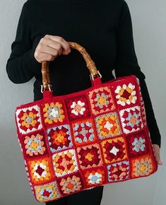 a woman holding a red crocheted bag with flowers on it and a bamboo handle