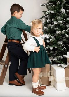 two young children standing in front of a christmas tree