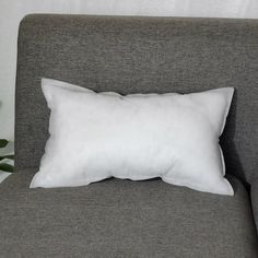 a white pillow sitting on top of a gray couch next to a potted plant