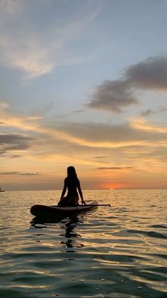 a woman sitting on top of a surfboard in the ocean at sunset or dawn