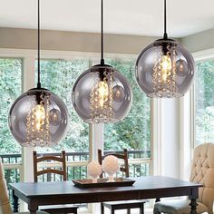 three glass globe lights hanging over a dining room table with chairs in front of it