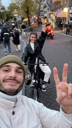 a man on a bike making the peace sign with his hand and two women standing behind him