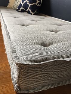 a close up of a mattress on a wooden floor near a wall with blue and white pillows