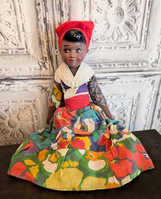 the doll is wearing a colorful dress and red headband, sitting on a black table