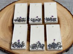 four bars of soap with lavender on them sitting on a wooden plate next to a gray table cloth