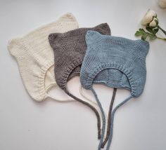 three knitted hats sitting next to each other on top of a white table with flowers