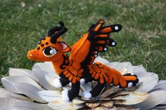 an orange and black dragon figurine sitting on top of a flower in the grass