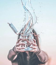 a woman is holding up a glass with water pouring out of it to her face