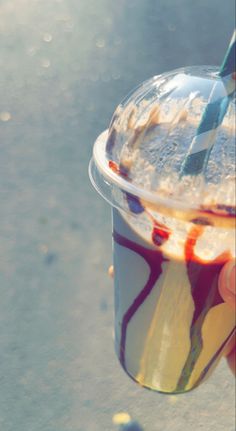 a hand holding a plastic cup with ice cream and toppings in it on the ground