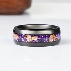 a purple and black wedding band with gold flowers on the inside is sitting on a white surface