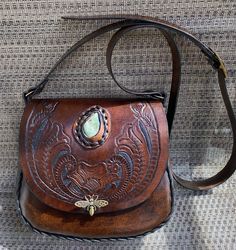 One of a kind handmade and hand tooled retro style leather handbag...the strap is adjustable and it can be worn as a shoulder or crossbody handbag...I tooled the flap and added a jade nugget ..the brass clasp is a unique bumble bee the size of this bag is 9 inches, 10 inches across, the gusset is 2 inches and the shoulder strap is21 when in the last hole.... Artisan Hand Tooled Crossbody Saddle Bag, Artisan Hand Tooled Crossbody Satchel, Bohemian Hand Tooled Leather Shoulder Bag, Unique Hand Tooled Brown Bag, Hand Tooled Brown Bag, Artisan Hand-tooled Crossbody Satchel, Unique Hand-tooled Brown Bag, Artisan Hand Tooled Leather Saddle Bag, Artisan Hand-tooled Leather Saddle Bag