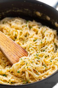 a wooden spoon in a skillet filled with spaghetti