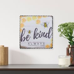 a wooden sign that says be kind with flowers on the table next to some vases