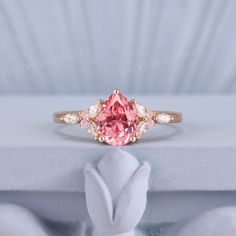 a pink diamond ring sitting on top of a white cloth covered box with its hands