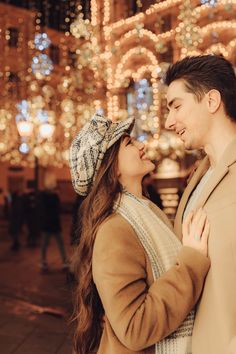 a man and woman standing next to each other in front of christmas lights