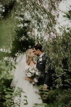 a bride and groom standing in the woods