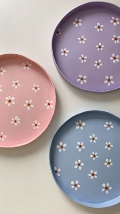 three plates with flowers painted on them, one is pink and the other is blue