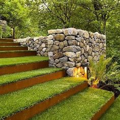 a stone wall next to some steps in the grass