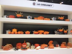 an assortment of orange dishes and pans on display in a room with white shelves