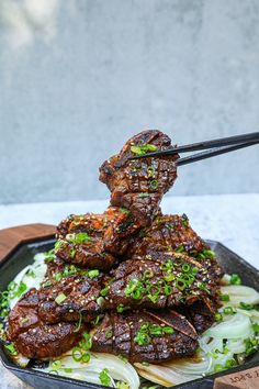 the meat is being served with chopsticks on top of noodles in a black bowl