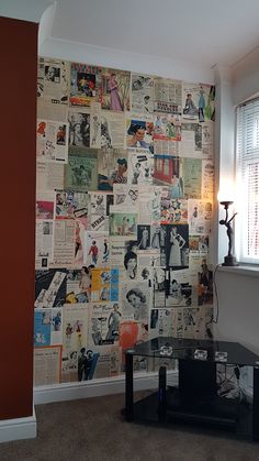 a living room with a wall covered in newspaper paper and a black coffee table next to a window