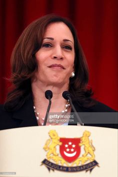 a woman standing at a podium in front of a red curtain with the emblem of australia on