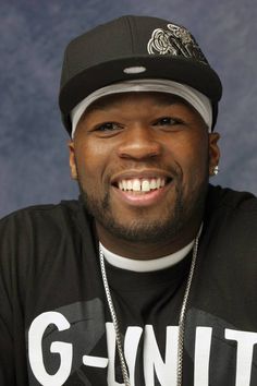 a man wearing a black shirt and hat smiling at the camera with his hand on his hip