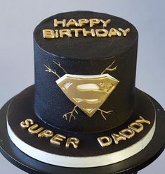 a black and gold birthday cake with a superman symbol on top