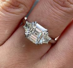 a woman's engagement ring with an emerald cut diamond in the center and two smaller diamonds on each side