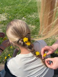 a woman sitting on the ground with two yellow flowers in her hair, and another person holding out their hand