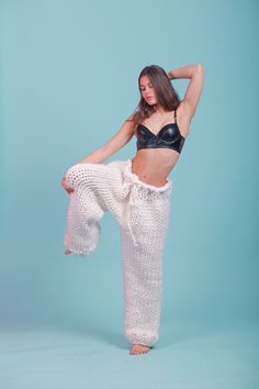 a woman in black bra top and white pants posing for a photo with her arms behind her head