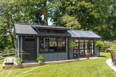 a small garden shed in the middle of a grassy area with a bench and potted plants