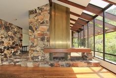 a stone fireplace in the middle of a room with wood flooring and large windows