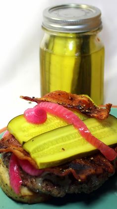 a bacon, cucumber and pickle sandwich is on a plate next to a jar of pickles