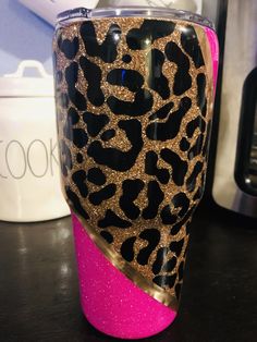 a pink and black tumbler cup with gold leopard print on the side sitting on a counter