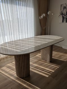 a table in the middle of a room with sheer curtains on the window sill