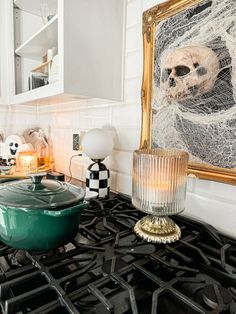 a green pot sitting on top of a gas stove next to a framed skull painting