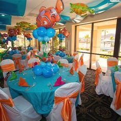 an ocean themed party with fish balloons and table cloths on the tables in front of large windows