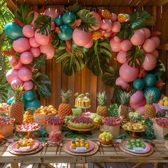 a table filled with lots of fruit and balloons in the shape of pineapples