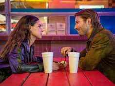 a man and woman sitting at a table with cups of food in front of them