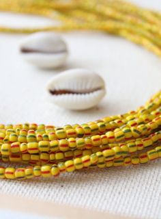 three strands of yellow and red seed beads on a white surface next to two seashells