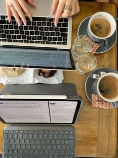 two people typing on their laptops at a table with cups of coffee and doughnuts