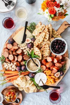 a platter filled with meats, vegetables and crackers next to glasses of wine